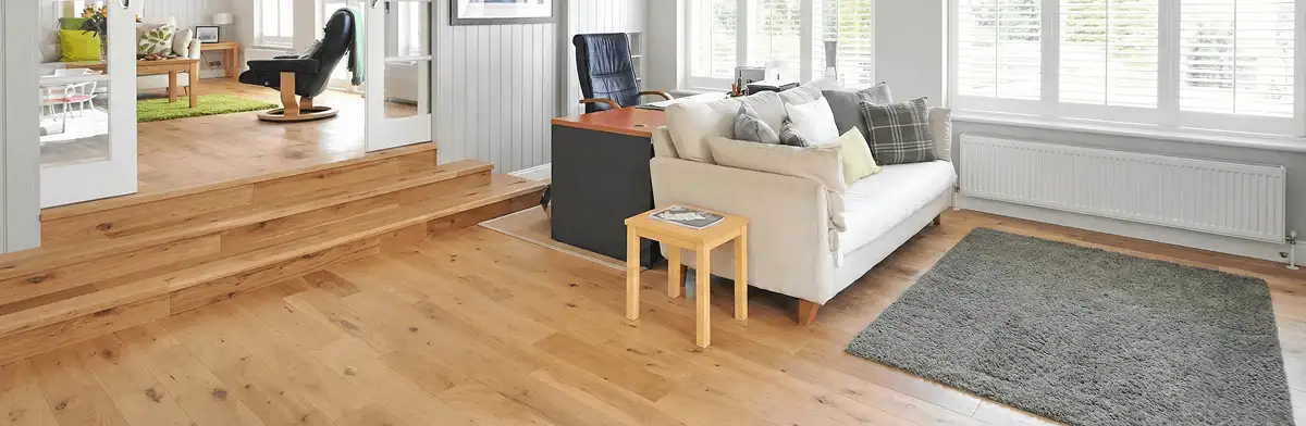 A modern living room with professionally installed laminate flooring, a beige sofa, a small side table, a gray rug, and large windows with white shutters in Staten Island, NY